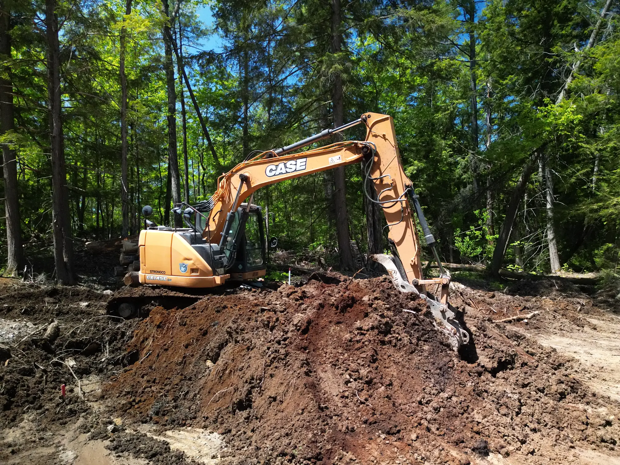 Excavator providing land clearing services on a wooded building lot.